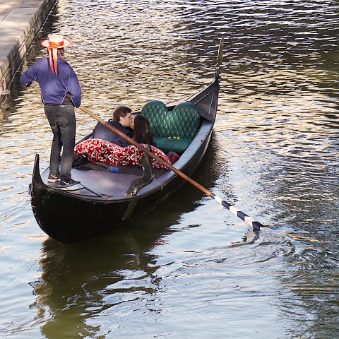 Couple in a gondola on a canal, gondolier steering with oar.