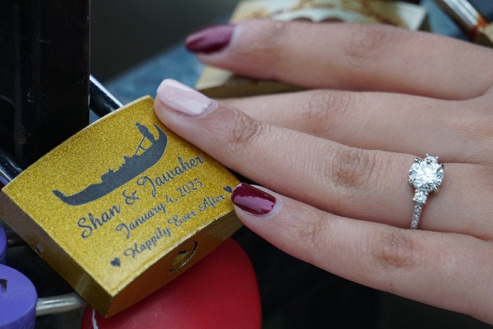 Woman's hand with ring on a love lock engraved with names and date.