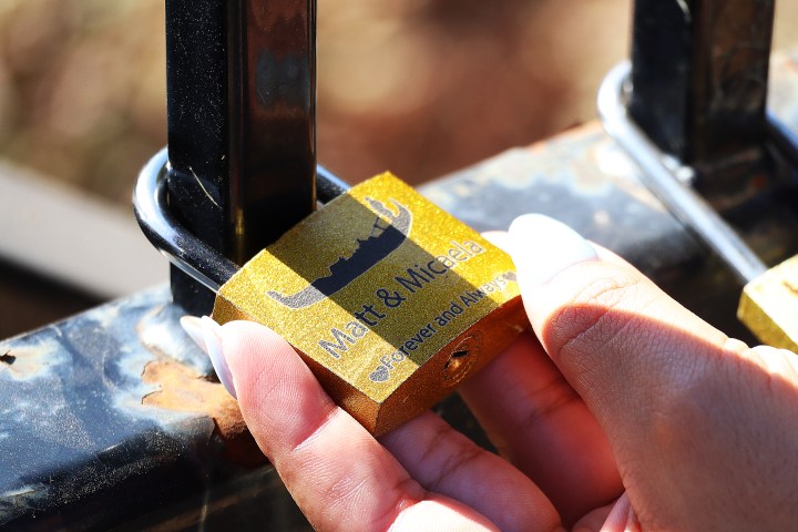Person holding a gold padlock attached to a fence.
