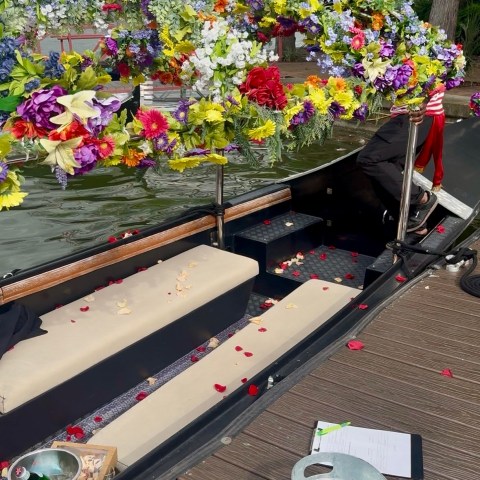 Flower-adorned boat docked, with a metal tub and clipboard on wooden deck.